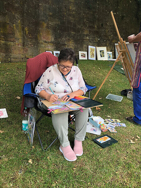 Hilde Bode sitzt auf einem Stuhl in einer Wiese und malt
