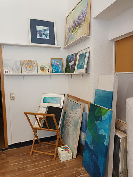 Mehrere gerahmte und ungerahmte Gemälde unterschiedlicher Größe lehnen an weißen Wänden und stehen auf dem Boden in einem Raum mit Holzboden